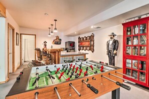 A room with a foosball table, a red cabinet with bottles, and a statue of a man in a suit. - Family Game Room: Spacious Overgaard Cabin (Overgaard)