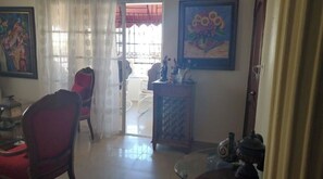 Un salon avec un fauteuil rouge, une table basse en verre et une porte donnant sur un balcon.