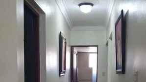 Un couloir aux murs blancs, doté d’un sol carrelé et d’une porte située sur le côté gauche.