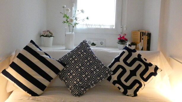 A bed with two pillows, a window with white curtains, and a small table with a potted plant. - Azhar Suites II (Córdoba)