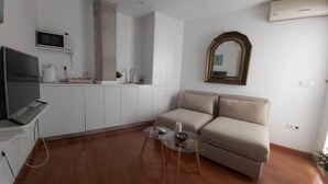 A modern living room with a sofa, a TV, a kitchen area, and a mirror. - Azhar Suites II (Córdoba)