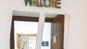 A torn paper cutout with a 'Welcome' sign and a door frame, revealing a hallway with a staircase and a sign reading 'ASHTA ASHRA'. - Azhar Suites II (Córdoba)