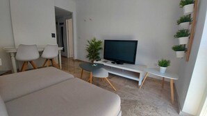 A modern living room with a flat-screen TV, a sofa, a dining table with chairs, and a small potted plant.
