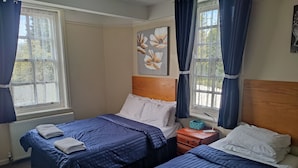 A bedroom with two beds, a wooden headboard, a painting of flowers, and a window with curtains. - Sussex Lodge Hotel (Slough)