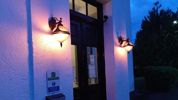 A building entrance with two wall-mounted lights and a sign indicating a smoking area. - Sussex Lodge Hotel (Slough)
