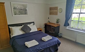 A bedroom with a bed, a desk, a chair, a clock, and a window with curtains.