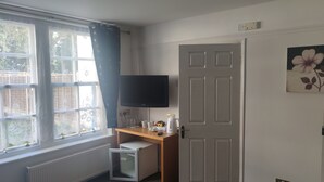 A room with a window, a desk, a television, and a door. - Sussex Lodge Hotel (Slough)