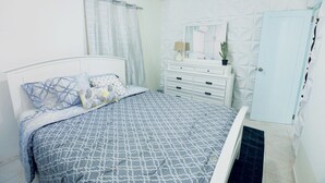 Un dormitorio con cama, cómoda, espejo, ventilador de techo y una puerta.
