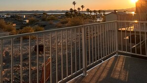 A balcony with a metal railing overlooking a desert landscape with sparse vegetation and distant mountains.