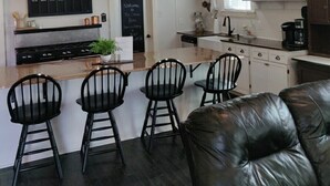A modern kitchen with a wooden ceiling, black pendant lights, a central island with bar stools, and a chalkboard menu. - The Conner House-Walk to Magnolia! (Waco)
