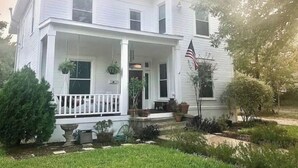 A two-story white house with a front porch, a flag, and a well-maintained garden. - The Conner House-Walk to Magnolia! (Waco)