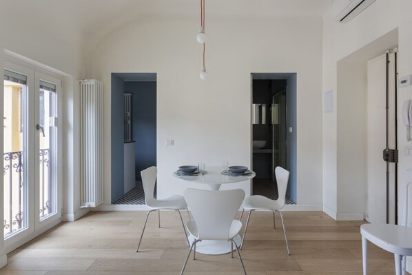 A modern dining area with a round table, white chairs, and a view of the kitchen.