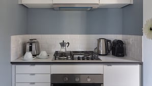 Une cuisine avec des meubles blancs, une cuisinière à gaz, une machine à café et une bouilloire.