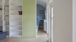 Une pièce avec une grande bibliothèque blanche, un lit avec une tête de lit bleue et un bureau avec une chaise.