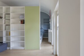 A room with a large white bookshelf, a bed with a blue headboard, and a desk with a chair.