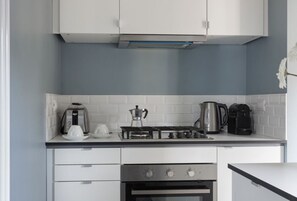 Cocina compacta con armarios blancos, estufa a gas, horno y cafetera.
