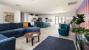 A modern living room with a blue sofa, a coffee table, and a kitchen in the background. - Revolution Retreat- Heated Pool 5 Mins to Old Town-Hidden Room (Scottsdale)