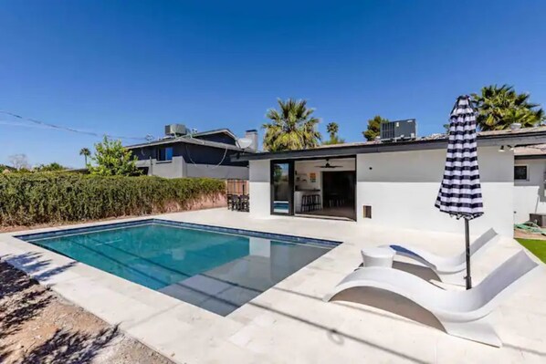 A modern house with a swimming pool, a covered patio, and a view of neighboring houses.