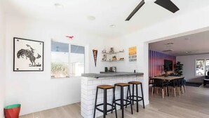 A modern kitchen with a white island, bar stools, and a dining area with a wooden table and chairs. - Revolution Retreat- Heated Pool 5 Mins to Old Town-Hidden Room (Scottsdale)
