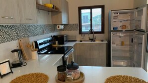 Une cuisine moderne avec des meubles blancs, un plan de travail noir, un four encastré et un réfrigérateur.
