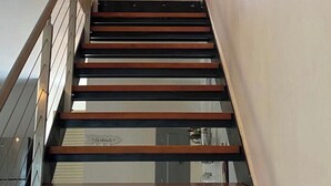 Un escalier avec des marches en bois et des rampes en métal, menant à un palier où est accrochée une peinture au mur.