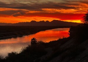Un coucher de soleil sur une rivière, avec des montagnes en arrière-plan.