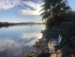 Une rivière paisible aux rives rocheuses, un palmier et un banc.