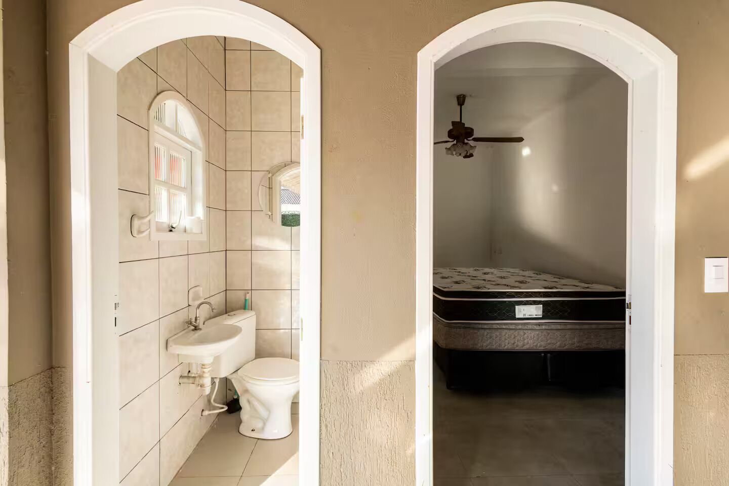 Ein Badezimmer mit Toilette, Waschbecken und Spiegel, sowie ein Schlafzimmer mit Bett und Deckenventilator.