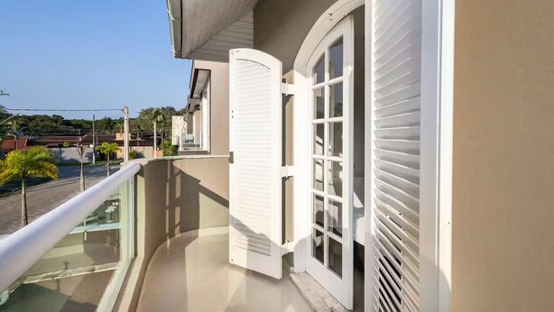Een balkon met glazen hekwerk, een witte deur en een raam met luiken.