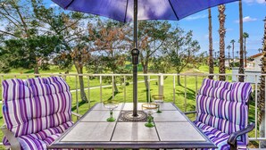 An outdoor patio with striped seating, a table, and a large umbrella. - Modern Desert Retreat: Luxurious Comfort & Endless Activities (Palm Desert)