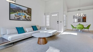 A modern living room with a white sofa, a round coffee table, and a painting of a pool. - Modern Desert Retreat: Luxurious Comfort & Endless Activities (Palm Desert)