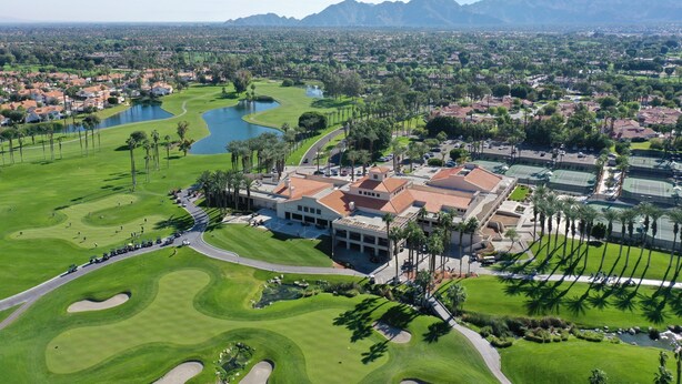 A golf course with a clubhouse, palm trees, and a lake. - Modern Desert Retreat: Luxurious Comfort & Endless Activities (Palm Desert)