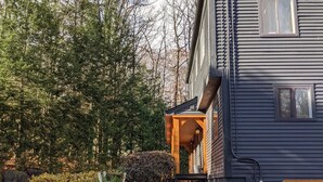 Ein Haus mit einer Steinstufe, die zu einer Holzveranda führt, umgeben von Bäumen und einem Garten.