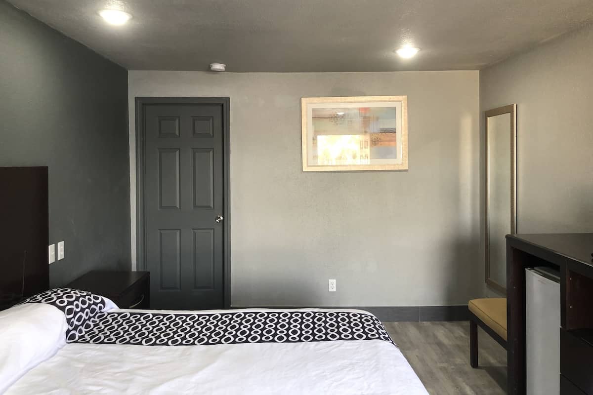 A bedroom with a bed, a door, a framed picture on the wall, and a mirror.