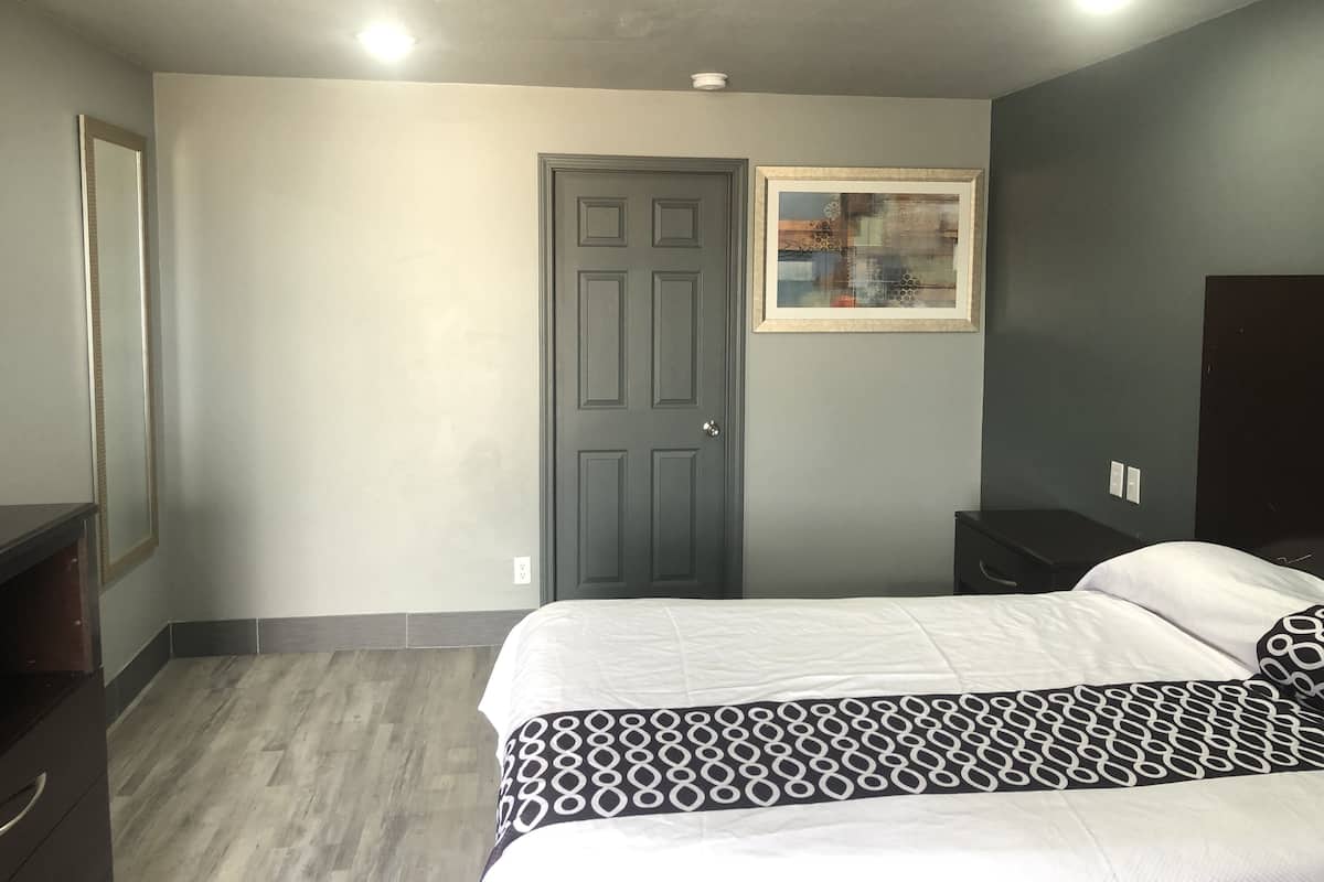 A bedroom with a bed, a door, a framed picture, and a dresser.