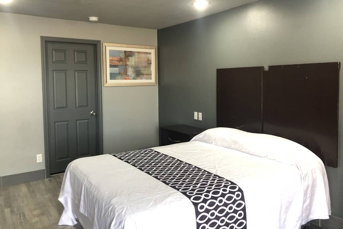 A bedroom with a bed, a door, a framed picture, and a dark-colored wardrobe.