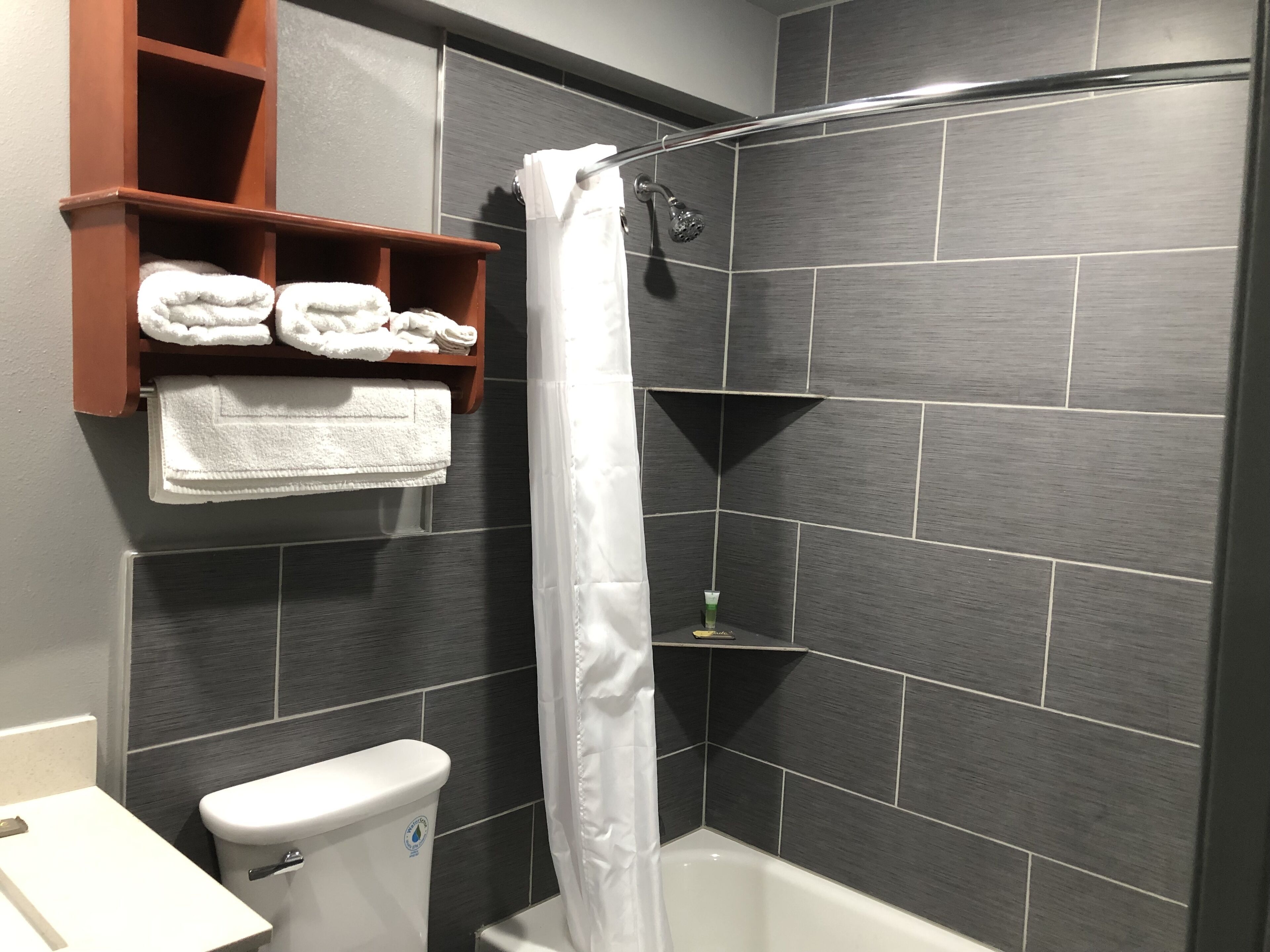 A bathroom with a shower, toilet, and a shelf with towels.