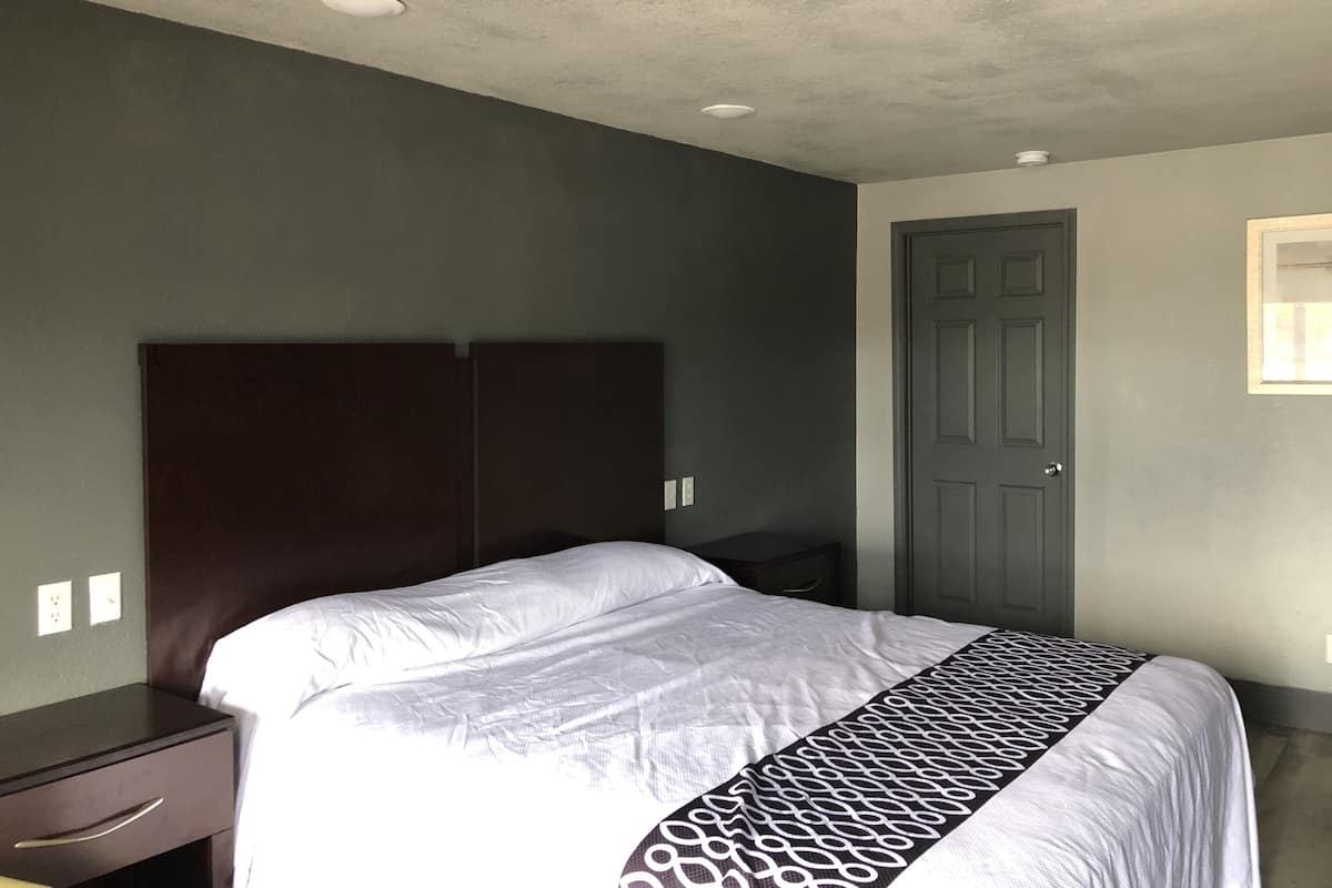 A bedroom with a bed, a nightstand, a dresser, and a door.