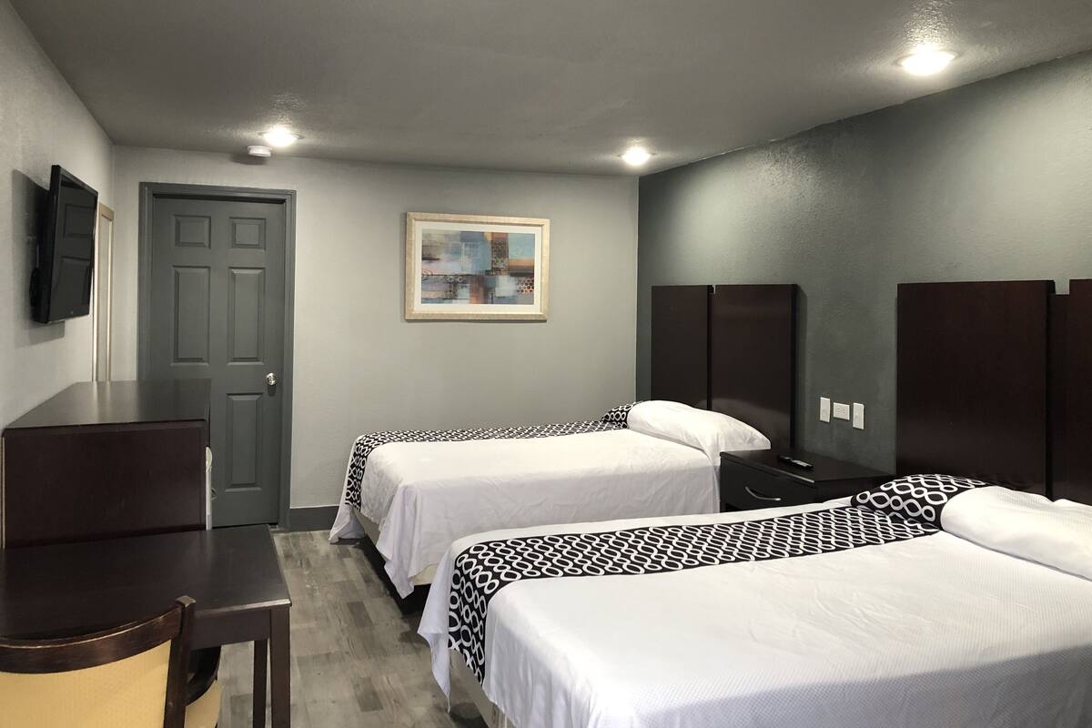 A hotel room with two beds, a desk, a chair, a TV, and a painting on the wall.