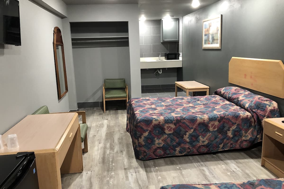 A compact hotel room with a bed, a chair, a small table, a microwave, and a sink.