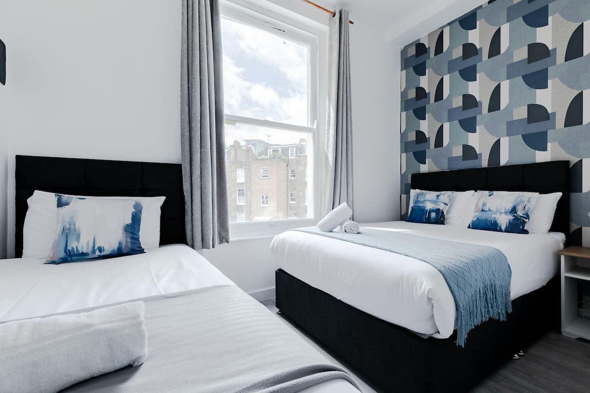 A modern hotel room with two beds, a large window, and a geometric patterned wall.