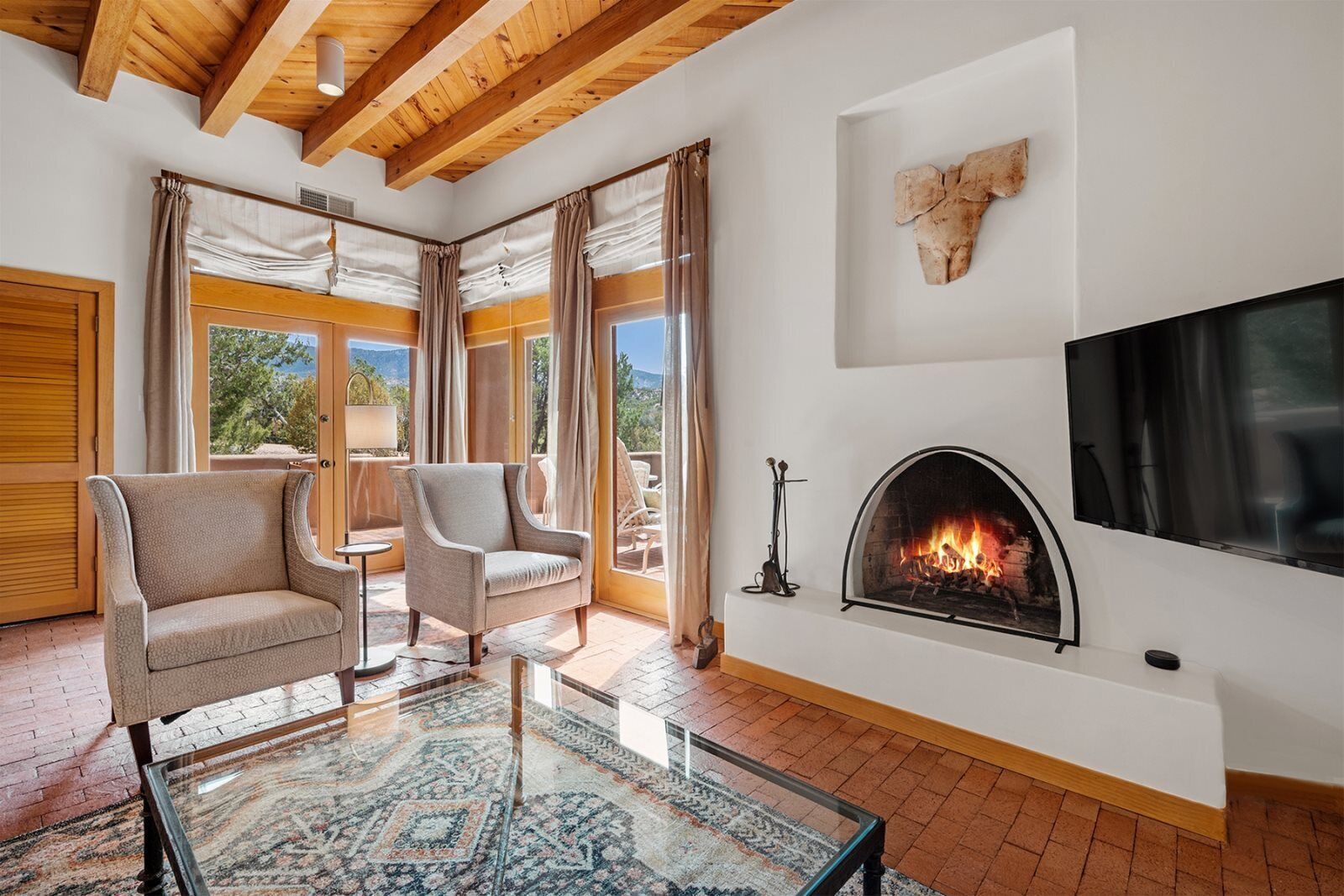A modern living room with a fireplace, large windows, and a mounted TV.