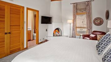 A bedroom with a large bed, wooden wardrobe, a fireplace, a TV, and a window with curtains.