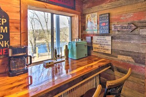 A rustic wooden bar area with a vintage coffee maker, a green suitcase, and a sign reading "Outhouse". - Lakefront Gem w/ Screened Porch + Game Room! (Shell Knob)
