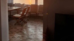 A room with a wooden floor, a sofa, and a table with chairs. There is a large window with a view of the sunset over the ocean. - WhiteStone Villa Mykonos with private pool (mykonos)
