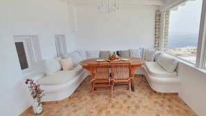 A corner room with a wooden dining table, white sofa, and a view of the sea. - WhiteStone Villa Mykonos with private pool (mykonos)