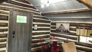A log cabin interior with a wooden door, a dining table with red chairs, a chandelier, and a bear picture on the wall. - Log Cabin on Lake Alice & ATV/UTV Trails, Papa Bear 2-Bedroom (Tomahawk)