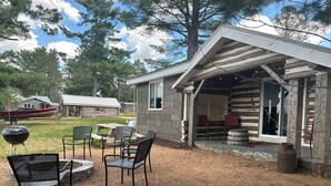 A rustic cabin with a covered porch, outdoor seating, and a boat in the background. - Log Cabin on Lake Alice & ATV/UTV Trails, Papa Bear 2-Bedroom (Tomahawk)
