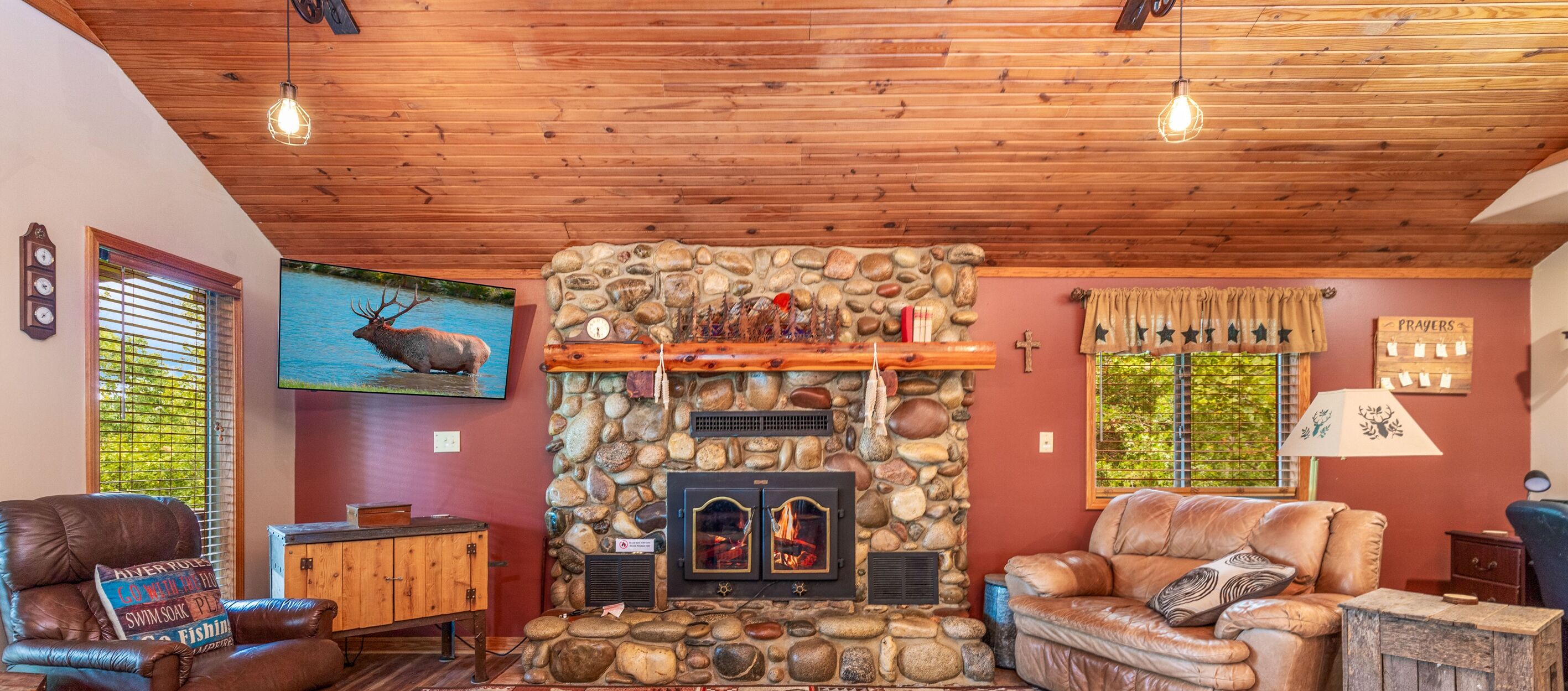 Una sala de estar acogedora con chimenea de piedra, muebles de cuero y televisión montada.