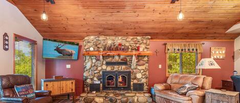 Una sala de estar acogedora con chimenea de piedra, muebles de cuero y televisión montada.